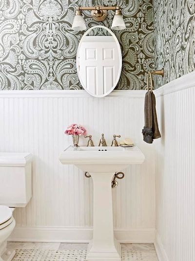 powder room with light gray & chocolate brown damask wallpaper, chair rail & beadboard, glossy white pedestal sink, marble tiles with marble basket weave inset tiles, oval pivot mirror and brass towel holder & frosted clear glass double sconce...